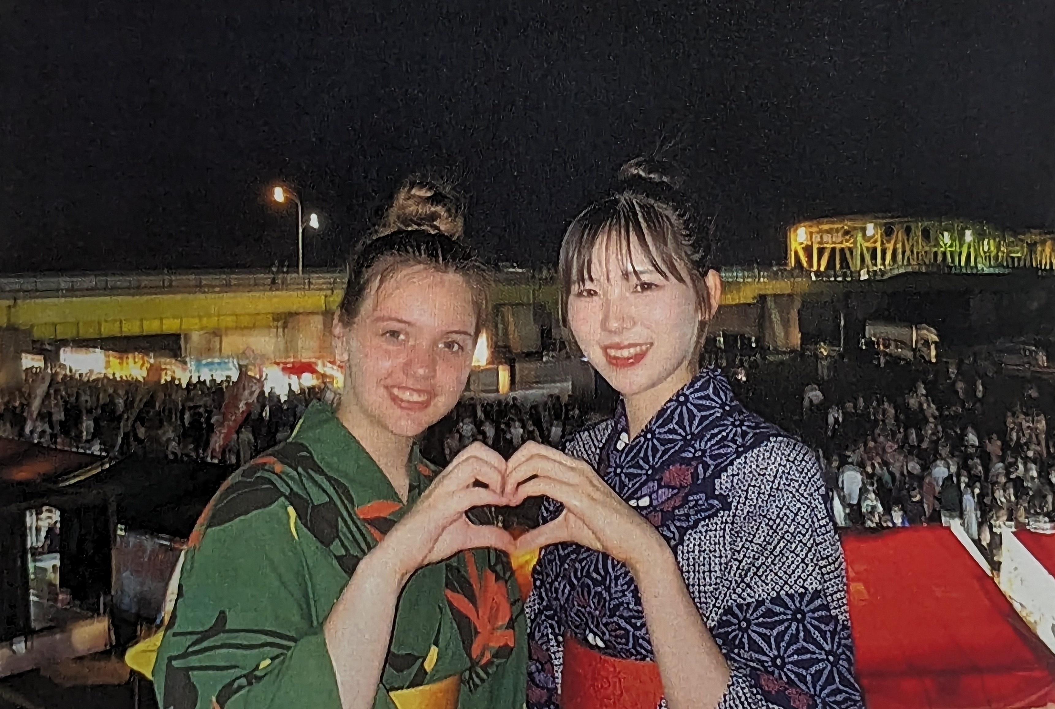 A young American girl with her Japanese friend making a heart with their hands.